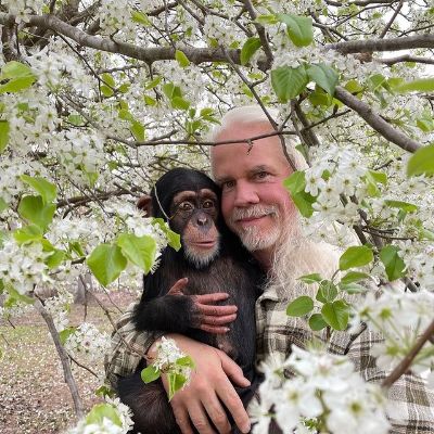 He is carrying the chimp as they are surrounded by white flowers.